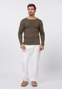 Khaki sweter z ribbingu, z długimi rękawami i szerokim dekoltem, w połączeniu z białymi spodniami i brązowymi sandałami. Teksturowana tkanina, casualowy design.