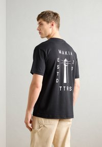 Must musta särk valge majaka graafika ja tekstiga seljal. Lühikesed varrukad ja ümmargune kaelus. LOOSE fit. Nähtavad õmbluse detailid.