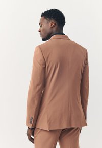 Veste de costume marron sur mesure vue de dos, présentant une texture lisse, des revers à cran et trois boutons sur chaque manchette.