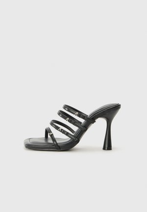 Mules noires à talons hauts avec quatre fines lanières et un bout carré. Fabriqués en cuir lisse avec des accents en métal argenté.