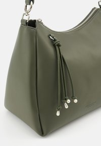 Olive green synthetic leather handbag with a structured shape, silver zipper, and decorative cords ending in pearl-like accents.