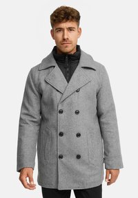 Grå uldblanding peacoat med dobbeltknaplukning, sorte knapper og sidelommer, lagdelt over en sort lynlåsjakke.