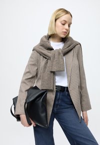 Καφέ σακάκι με μοτίβο houndstooth, γκρι κασκόλ περασμένο στους ώμους, λευκό μπλουζάκι, σκουρό μπλε τζιν, κρατώντας μια μαύρη δερμάτινη τσάντα.