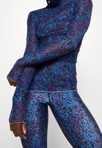 Pitkähihainen urheiluämpäri ja siihen sopivat legginssit purppurassa ja sinisessä leopardikuosisessa, joissa on istuva muotoilu ja peukalonreikäkädenhihnat.