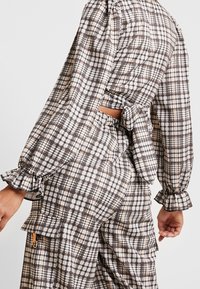 Kariertes Zwei-Teile-Outfit in Braun, Weiß und Beige, mit Puffärmeln, einem Ausschnitt und gerafften Akzenten mit Rüschensäumen.