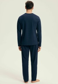 Niebieska, paskowana bluzka z długim rękawem w połączeniu z dopasowanymi niebieskimi spodniami, wykonanymi z miękkiego materiału, o luźnym kroju i otwartych mankietach.