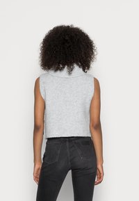 Pull gris court à col montant, texture côtelée et sans manches. Associé à un jean noir taille haute dans un style décontracté.