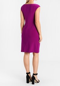 Abito attillato in tessuto viola vivace, senza maniche e con una texture morbida. Il retro presenta un sottile dettaglio di cucitura. Sandali neri con tacco alto mostrati.