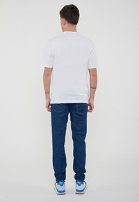 T-shirt bianco a maniche corte, jeans in denim blu e scarpe da ginnastica grigie con dettagli blu. I jeans presentano cuciture sulle tasche posteriori. Design semplice e casual.