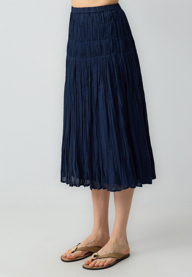 Gonna maxi plissettata blu navy con vita smock, realizzata in tessuto leggero, caratterizzata da una texture fluida e un design alla caviglia.