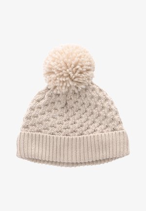 Kremo spalvos megzta žieminė kepurė su dideliu pūkuotu bumbulu viršuje ir ribinėta sulenkta apačia.