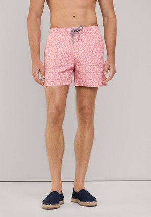Shorts de bain roses avec un motif floral et un cordon de serrage noir et blanc ajustable. Portés avec des espadrilles bleu marine.