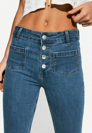 Hoch taillierte blaue Denim-Jeans mit fünf metallicfarbenen Knöpfen, zwei Vordertaschen, Kontrastnähten und einem schmalen Schnitt.