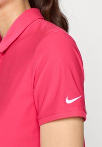 Rózsaszín Nike polo ing, galléros nyakkal, rövid ujjú és fehér logóval a bal ujján. Simának és könnyűnek mondható anyag.
