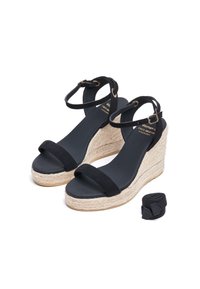 Zwarte suede wedgesandalen met een jute platform, voorzien van een brede band over de tenen en een enkelbandje met een gouden gesp. Inclusief een zwarte strik.
