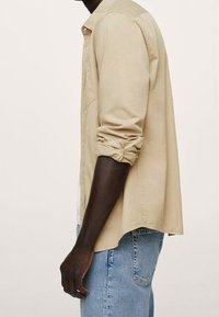 Chemise de couleur crème avec manches retroussées, fermeture boutonnée à l'avant et coupe décontractée. Associée à un jean en denim bleu clair, mettant en avant un style décontracté.