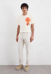 Cream t-shirt with orange floral graphic, paired with light beige pants and tan shoes. Casual fit, cotton material, and smooth texture.