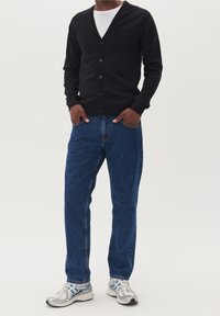 Černý pletený kardigan s výstřihem do V a šesti knoflíky, spárovaný s modrými džíny a stříbrnými teniskami s modrými akcenty.