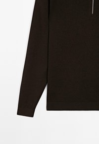 Dunkelbrauner Pullover mit langen Ärmeln, Rippenbündchen und -saum, der im oberen rechten Bereich einen teilweisen Blick auf einen silbernen Reißverschluss bietet.