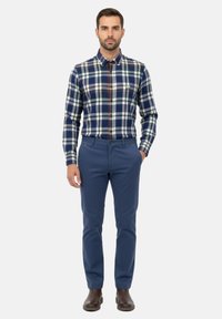 Camisa de cuadros en azul marino, verde y blanco con detalles en marrón, combinada con pantalones azul marino. Textura suave y diseño de cuello clásico.