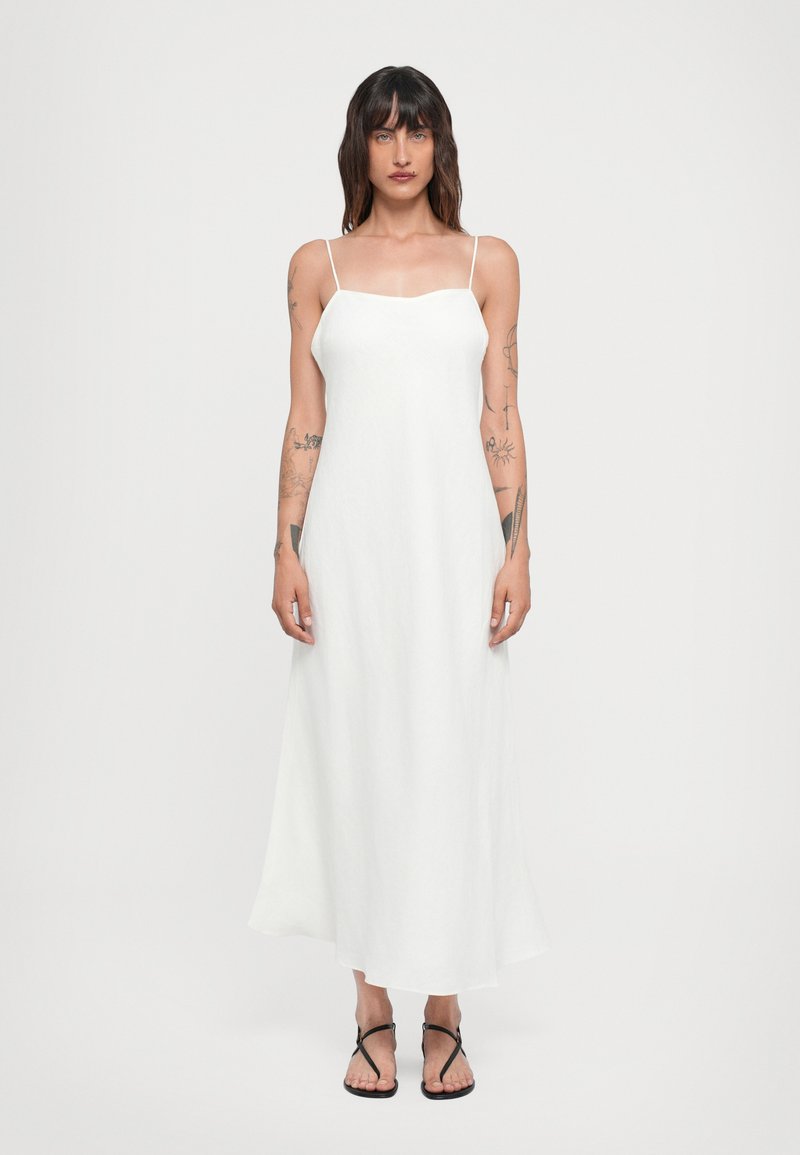 Vestido maxi blanco sin mangas con tirantes finos, escote recto y silueta fluida; combinado con chanclas negras.
