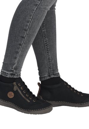 Black leather ankle boots with a round toe, textured sole, gold zipper, and stitching details, worn with gray skinny jeans.