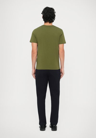 Λαδί κοντομάνικο μπλουζάκι με στρογγυλή λαιμόκοψη, συνδυασμένο με σκούρο μπλε παντελόνι. Το ύφασμα φαίνεται λείο με εφαρμοστή γραμμή, μινιμαλιστικό στυλ.