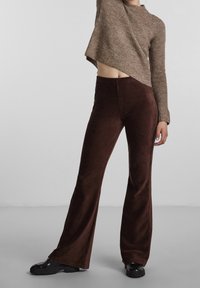 Braune Cord-Streifenhosen mit strukturierter Oberfläche, kombiniert mit einem cropped braunen Strickpullover. Schwarze Plateauschuhe vervollständigen das Outfit.