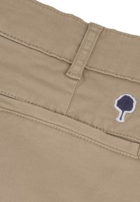 Ceinture en tissu beige avec des accents cousus et un petit logo d'arbre brodé en bleu marine. Le matériau semble durable et lisse.