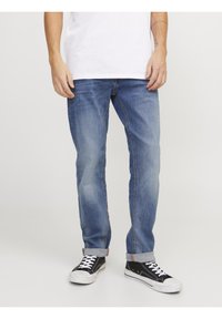 Jean en denim bleu clair avec une coupe droite, un léger délavage et des ourlets retroussés, associés à des baskets noires avec des lacets et des semelles blanches.