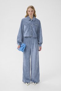 Jasnoniebieski dżinsowy strój składający się ze skróconej kurtki zapinanej na guziki z dwoma kieszeniami na piersi oraz szerokich, wysokowistednich spodni. Trzyma niebieską torebkę.