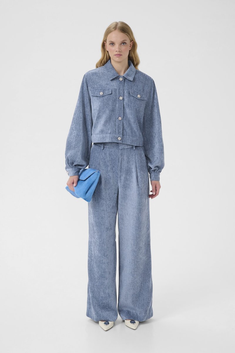 Light blue denim outfit featuring a cropped button-up jacket with two chest pockets and wide-leg, high-waisted pants. Holds a blue handbag.