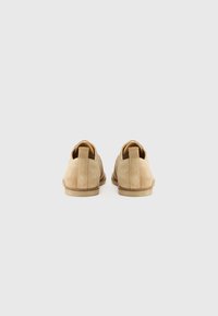 Zapatos de ante beige con un tacón bajo, que presentan una punta redondeada y una costura a lo largo de la parte trasera. Diseño sencillo con una textura suave.