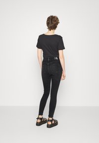 Jeans skinny negros de cintura alta con cinco bolsillos y detalles de costura en contraste, combinados con una camiseta negra lisa y sandalias negras.