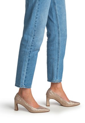 Beige laklæder højhælede pumps med spids tå, med en tekstureret finish og en blokhæl. Kombineret med korte blå cowboybukser.