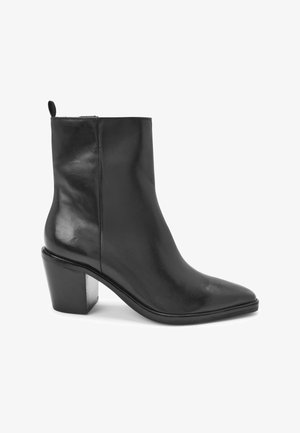 Bottine en cuir noir avec bout pointu, fermeture éclair latérale, talon bloc et languette à l'arrière.