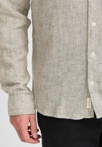 Krave skjorte lavet af let, struktureret stof med tynde lodrette striber i beige og grå, med knapper og et sideetiket.