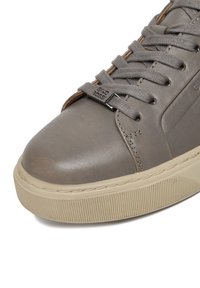 Grauer Ledersneaker mit strukturierten Details, runder Spitze, Schnürsenkeln und einer Gummisohle mit geriffeltem Design. Markenlogo an der Seite.