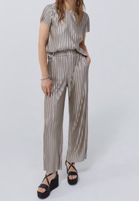 Conjunto de dos piezas de satén a rayas en color taupe claro, con una blusa de corte suelto y pantalones con cintura elástica. Sandalias de plataforma negras con tiras cruzadas.