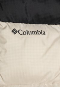 Veste Columbia avec une partie supérieure noire et une partie inférieure crème ornée d'un motif en grille, logo de la marque sur le tissu crème, texture matelassée.