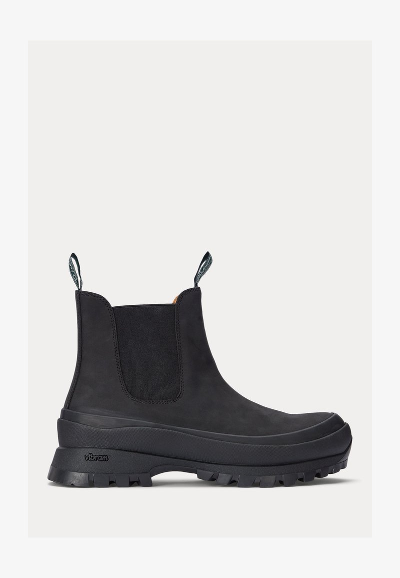 Botas Chelsea impermeables negras de goma, con paneles elásticos texturizados a los lados y lengüetas en la parte trasera. Presentan una suela gruesa con dibujo para mayor tracción.