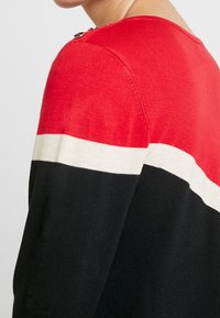 Gestreifter Pullover in Rot, Weiß und Schwarz mit Rundhalsausschnitt und Schulterknöpfen. Das Material ist weich und gestrickt.