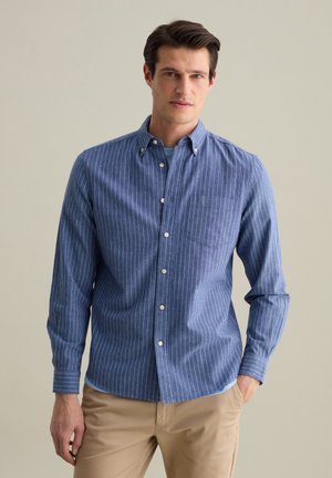 Camisa de botones a rayas azules con cuello, bolsillo frontal y mangas largas, confeccionada en una tela tejida con una textura suave.