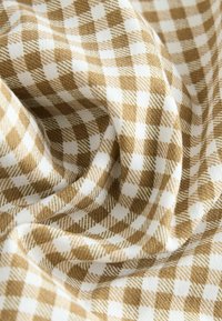 Tissu à carreaux vichy marron et blanc avec une texture douce, présentant un motif de carreaux classique et une apparence drapée.