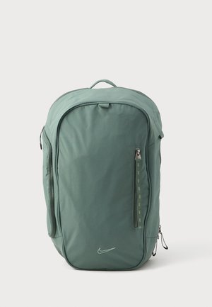 Sac à dos en nylon vert avec une forme arrondie, une poignée supérieure, des compartiments zippés et un petit logo Nike à l'avant.