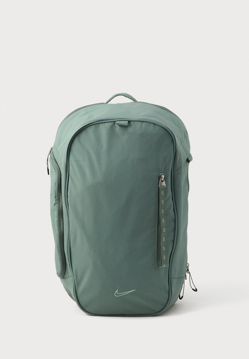 Zelený nylonový batoh s zaobleným tvarom, vrchnou rukoväťou, zipsovými priehradkami a malým logom Nike na prednej strane.