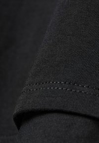 Černá bavlněná tkanina s hladkým povrchem, s přehnutým lemem a pečlivě provedeným švem. Pohled zblízka na rukáv oděvu.