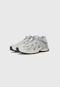 Lightweight athletic shoes in pale gray and white mesh, featuring a unique wavy design, cushioned sole, and elastic laces for secure fit.