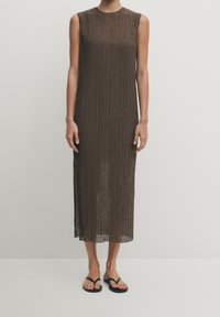 Ruskea ribbikuvioinen hihaton mekko, jossa on suora siluetti, polven puoliväliin asti ulottuva pituus ja kevyt, pinta-textuuria omaava kangas. Yhdistetty mustiin flip-flop -sandaaleihin.