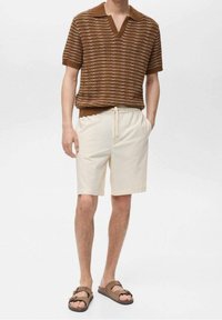 Hnědý pruhovaný pletený polokošile s výstřihem do V, kombinovaná s béžovými šortkami na šňůrku a hnědými sandály. Hladká tkanina a uvolněný design.